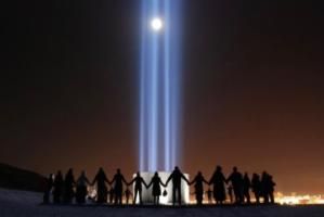 A group of people hold hands around the Imagine Peace tower on Videy island.
