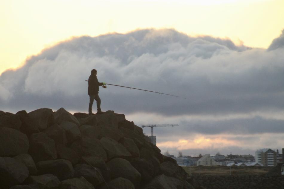 fisherman reels a rod from the harbour walls