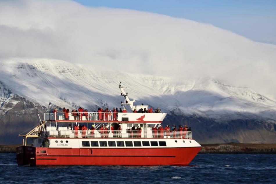 hafsúlan boat sailing home with passengers from a whale watching cruise in reykjavik iceland with esjan mountain in the background a stormy sea and some clouds