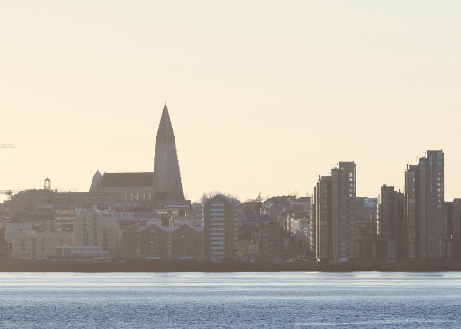 Reykjavík city view from the sea in winter, with orange hues across the sky and blue seas underneath.